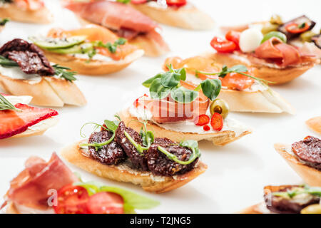 Selektiver Fokus der italienischen Bruschetta mit getrockneten Tomaten, Schinken und Kräutern auf Weiß Stockfoto