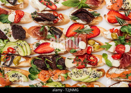 Hintergrund der italienischen Bruschetta mit Lachs, Schinken, Erdbeeren, getrockneten Tomaten und Kräutern isoliert auf weißem Stockfoto