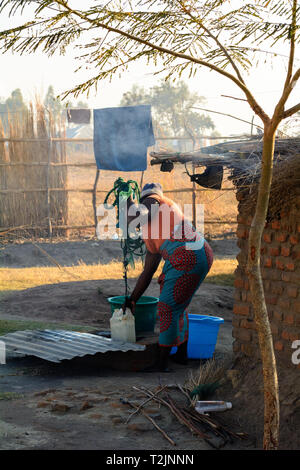 Malawische Frau zieht Wasser aus flachen gut mit einem Kunststoffbehälter Stockfoto