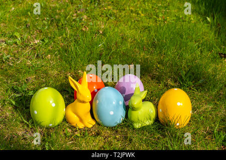 Bunte Keramik Ostereier und Osterhasen auf einer Wiese. Stockfoto