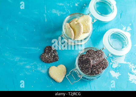Köstliche gebackene Herzförmige Schokolade und Keks Plätzchen mit Kokos Chips in Gläsern auf blauen Beton Tabelle Oberfläche. Essen Grußkarte mit Co Stockfoto