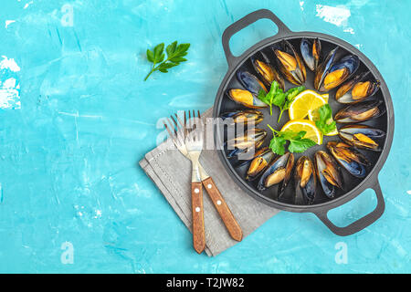 Meeresfrüchte Miesmuscheln mit Zitrone und Petersilie in Black Metal pan auf Blau konkrete Tischfläche, Ansicht von oben, kopieren Sie Text Stockfoto