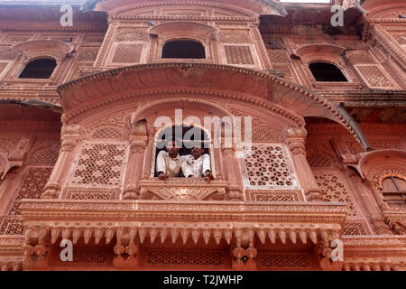 Zwei Einheimische aus einem reich verzierten Stein Fenster in Mehrangarh, Mehran Fort, Jodhpur, Rajasthan, Indien Stockfoto