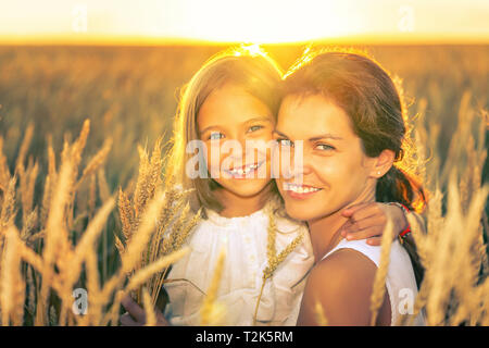 Junge Frau und ihre Tochter auf goldenen Weizenfeld am sonnigen Sommerabend. Stockfoto