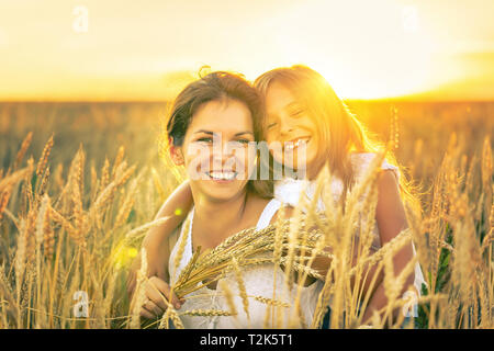 Junge Frau und ihre Tochter auf goldenen Weizenfeld am sonnigen Sommerabend. Stockfoto