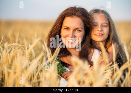 Junge Mutter und ihre Tochter auf goldenen Weizenfeld bei sommerlichen Abend. Stockfoto