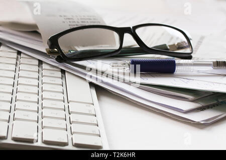 Computer Tastatur, Brille, Bleistift und unordentliche Papiere liegen auf einem weißen Tisch Stockfoto