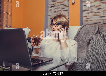 Frau mittleren Alters zum Telefonieren und mit Laptop zu Hause. - Bild Stockfoto