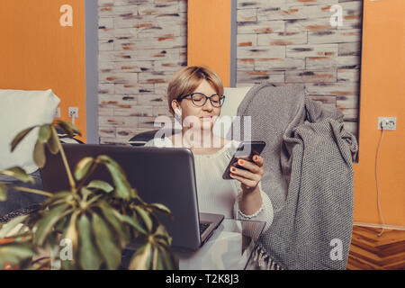 Frau mittleren Alters mit Smartphone und Arbeiten am Laptop zu Hause. - Bild Stockfoto