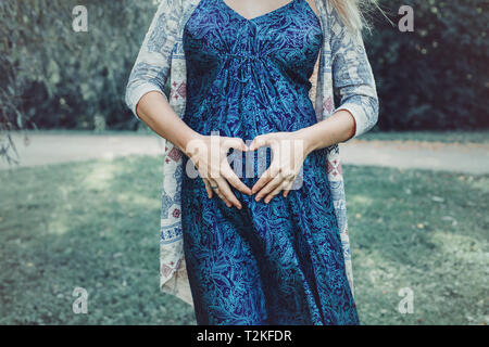 Closeup Körper der weißen Kaukasischen schwangere Frau ihren Bauch und Herz Form mit den Fingern mit den Händen berühren. Erwartet junge weibliche Mutter in p Posing Stockfoto