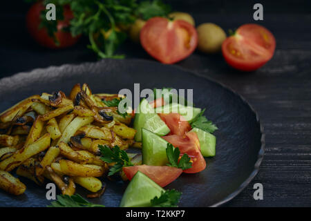 Frisch gebratene Kartoffeln mit Zwiebeln und Pilze close-up auf einem Teller gekocht. schwarz Holz Tisch. Horizontale Stockfoto
