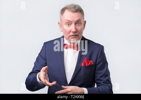 Freundlich älterer Mann im blauen Anzug duscussing Frage mit ihnen mit offenen Händen Geste und lächelte Kamera Stockfoto