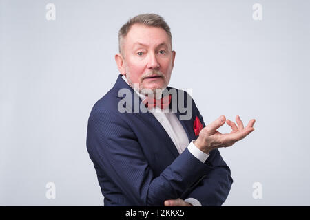 Freundlich älterer Mann im blauen Anzug duscussing Frage mit ihnen mit offenen Händen Geste und lächelte Kamera Stockfoto
