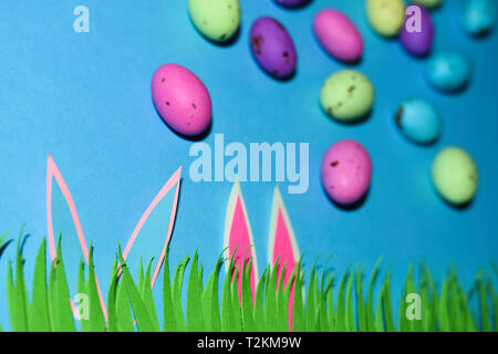 Rabbit Ears mit Gras und Candy Eier auf Blau Stockfoto