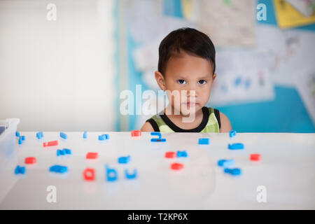 Junge Schwierigkeiten beim Lernen in einem Kindergarten mit Buchstaben des Alphabets auf dem Schreibtisch. Stockfoto