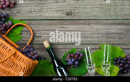 Weinflaschen mit Trauben, Korb, zwei Weingläser auf Holz- Hintergrund. Ansicht von oben Stockfoto