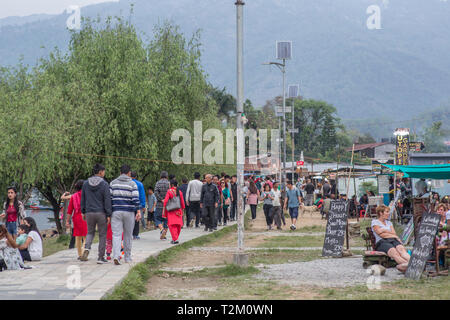 Menschen zu Fuß entlang der Spaziergang weg neben dem berühmten See in Pokhara, während einige Touristen sitzen auf der Restaurants und Cafés. Stockfoto