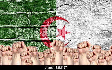 Männliche Hände umklammerten in der Faust, vor dem Hintergrund einer zerstörten Mauer mit einer Flagge Algerien angehoben. Das Konzept der Arbeiterbewegung aus Stockfoto