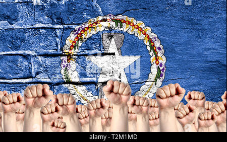 Männliche Hände umklammerten in der Faust, vor dem Hintergrund einer zerstörten Mauer mit einer Flagge von Nördliche Marianen angehoben. Das Konzept der Übung. Stockfoto