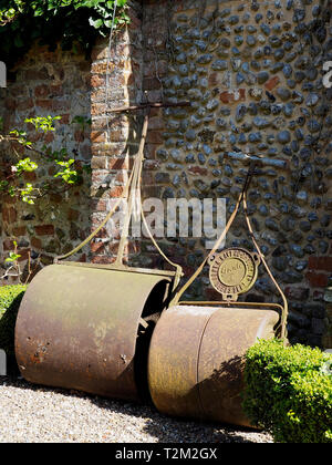 Zwei große möglicherweise viktorianische gusseiserne Garten Rollen lehnte sich gegen a8r und Feuerstein Garten Wand. Stockfoto