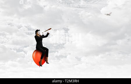 Mime-Frau im schwarzen Anzug sitzt auf Ballon. Mixed Media Stockfoto