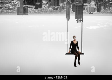 Frau mime im schwarzen Anzug sitzt auf Swing. Mixed Media Stockfoto