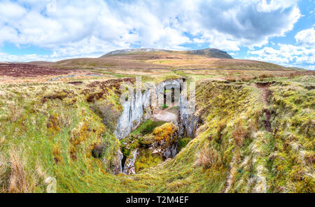 Ein grosser Felsen Schlucht mit massiven Klippen in einer kargen, grünen Landschaft ist unter dem Gipfel des Pen-y-Gent im Peak District, England gesehen. Stockfoto