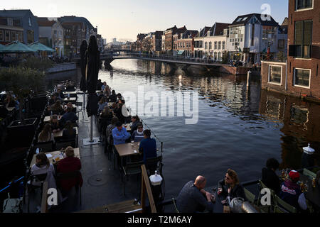 Eine Gruppe von Leuten, die etwas Trinken auf einer der Terrassen in einer der wichtigsten Kanäle, die die Stadt Leiden Kreuz entfernt sitzen. Stockfoto