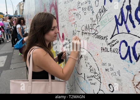 Berlin. Deutschland. Eine junge Frau, die ihre Markierung an der Berliner Mauer an der East Side Gallery. Stockfoto