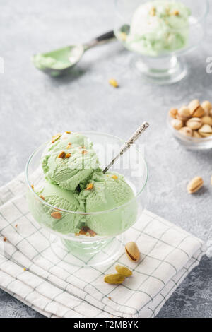 Pistazieneis in eine Schüssel mit gehackten Nüssen auf grauem Hintergrund. Sommer dessert Konzept. Stockfoto