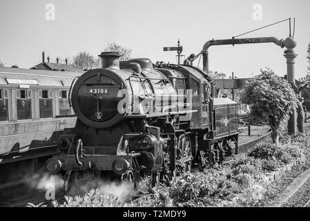 Schwarz-weiß Nahaufnahme der alten britischen Dampflok, vorne, in den Anschlussgleisen, die Wasser aufnehmen. Dampfzugbesatzung, Fahrer & Feuerwehrmann, betreiben Wasserkran. Stockfoto