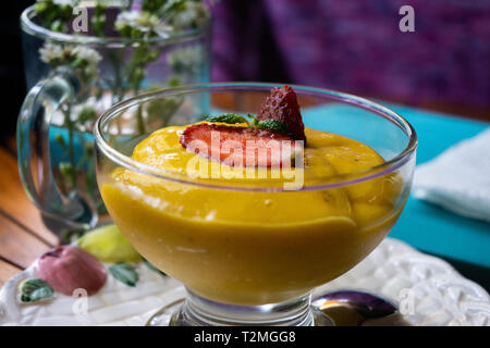 Steigern Sie Ihren Tag mit frischen Bio mango Saft mit minzeblatt auf der Oberseite. Es dient auf dem Holz runder Tisch Stockfoto