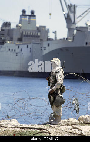 30. Oktober 1993 einen schwarzen US-Armee Soldat des 24 Infanterie Division, 1.BATAILLON der 64th Armored Regiment, steht am Rand des Wassers in den neuen Hafen in Mogadischu, Somalia. Im Hintergrund ist der riesige United States Marine Verwaltung Fahrzeug Frachtschiff, USNS Denebola. Stockfoto