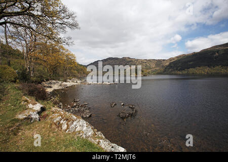 Angler auf der felsigen Küstenlinie von Loch Lomond mit Laub- und Nadelholz Wald auf den fernen Hügel Loch Lomond und der Trossachs National Park Sc Stockfoto