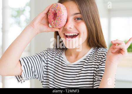 Schöne junge Mädchen Junge Süßigkeiten rosa Donut sehr zufrieden zeigt mit Finger- und an der Seite Stockfoto