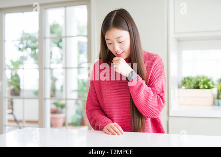 Schöne asiatische Frau rosa Pullover am weißen Tisch Unwohlsein und als Symptom für kalte oder Bronchitis Husten. Healthcare Konzept. Stockfoto