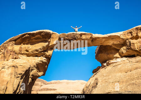Berühmte um Frouth rock Arch, im Wadi Rum Wüste in Jordanien. Reisender Fotograf mit offenen Armen posiert für ein Erinnerungsfoto. Glück der werden.
