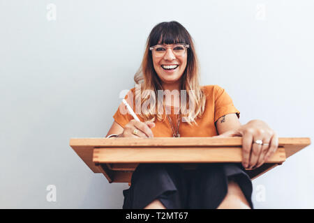 Nahaufnahme eines weiblichen Künstler sitzen mit einem Zeichenbrett und Arbeiten. Lächelnd weibliche Künstler sitzen mit einer Zeichnung pad auf den Knien halten Sie einen Stift in h Stockfoto