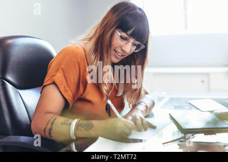 Seitenansicht eines weiblichen kreativer Künstler eine Zeichnung auf Papier saß an ihrem Schreibtisch. Nahaufnahme eines Geschäftsfrau schreiben auf ein Papier. Stockfoto