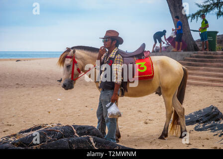 Songkhla, Thailand - Okt 2015: Mann mit einem Pferd an den populären Samila Strand posiert, Thailand Stockfoto