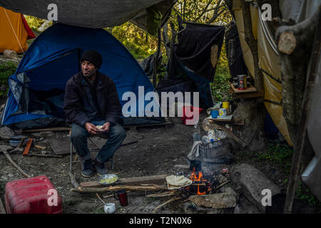 Vathy, Griechenland. 25 Mär, 2019. Am offenen Feuer wärmen sich Flüchtlinge im Camp auf der griechischen Insel Samos. Rund 4500 Flüchtlinge und Migranten leben hier. Sie wurden gezwungen, um die Insel zu vereinbaren so genannte Hotspot, einem ehemaligen Gefängnis, das sich hinter der Stahl Zäune mit Stacheldraht bewehrt, bietet Platz für 650 Personen. Credit: Angelos Tzortzinis/dpa/Alamy leben Nachrichten Stockfoto