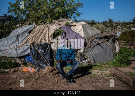 Vathy, Griechenland. 25 Mär, 2019. Ein Flüchtling sitzt in einem Flüchtlingslager auf der griechischen Insel Samos vor seinem Zelt. Rund 4500 Flüchtlinge und Migranten leben hier. Sie wurden gezwungen, um die Insel zu vereinbaren so genannte Hotspot, einem ehemaligen Gefängnis, das sich hinter der Stahl Zäune mit Stacheldraht bewehrt, bietet Platz für 650 Personen. Credit: Angelos Tzortzinis/dpa/Alamy leben Nachrichten Stockfoto