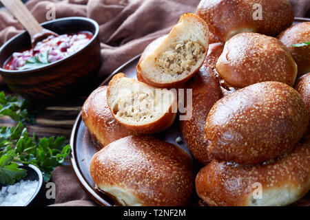 Frisch gebackenes Brot Teig Brötchen mit Boden Schweine- und Hühnerfleisch füllen, portablen Pocket Sandwiches auf einem Schild an einem Holztisch mit braunen Tuch und Stockfoto