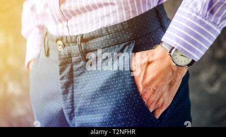 Nahaufnahme der männlichen Hand in der Hosentasche mit eleganten Armbanduhr. Kaukasische Geschäftsmann in gestreiften Hemd tragen stilvolle Kleidung aufpassen. Mode und Punctua Stockfoto