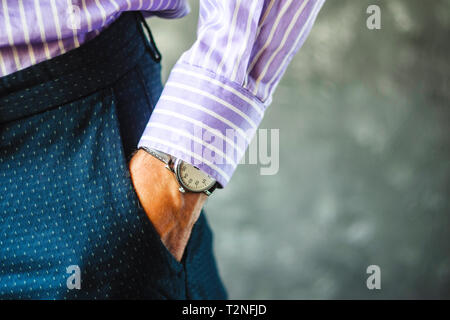Nahaufnahme der männlichen Hand in der Hosentasche mit eleganten Armbanduhr. Kaukasische Geschäftsmann in gestreiften Hemd tragen stilvolle Kleidung aufpassen. Mode und Punctua Stockfoto