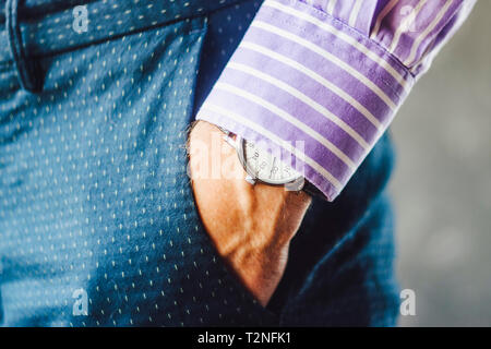 Nahaufnahme der männlichen Hand in der Hosentasche mit eleganten Armbanduhr. Kaukasische Geschäftsmann in gestreiften Hemd tragen stilvolle Kleidung aufpassen. Mode und Punctua Stockfoto