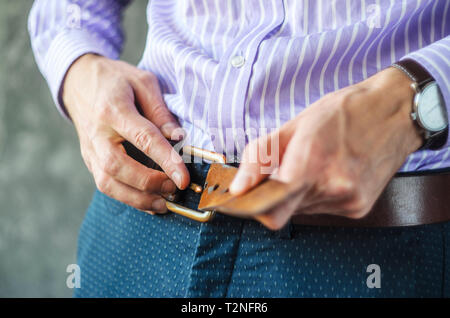 Junger Mann im gestreiften Hemd setzt an einem Riemen in der Hose. Auf Kleidung Konzept Stockfoto