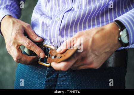 Junger Mann im gestreiften Hemd setzt an einem Riemen in der Hose. Auf Kleidung Konzept Stockfoto