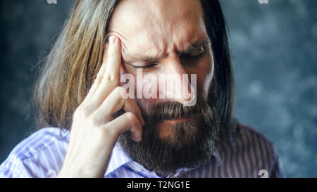 Der bärtige Mann mit dem langen Haar massieren sein Recht Tempel mit seinen Fingern. Kopfschmerzen Konzept. Nahaufnahme Stockfoto