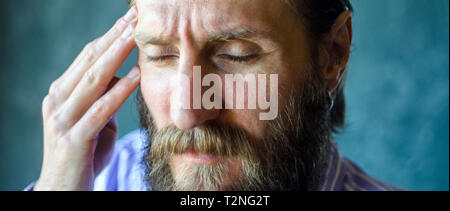 Close-up Portrait von Angesicht geschlossene Augen eines Mannes Leiden Kopfschmerzen Symptom der Krankheit. Bärtiger Mann massiert seine Rechte Tempel mit seinen Fingern. Wr Stockfoto